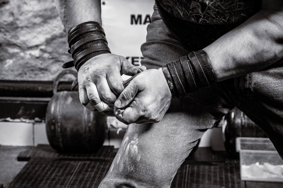 Chalked hands with leather wrist wraps, a lifter working chalk in before a set