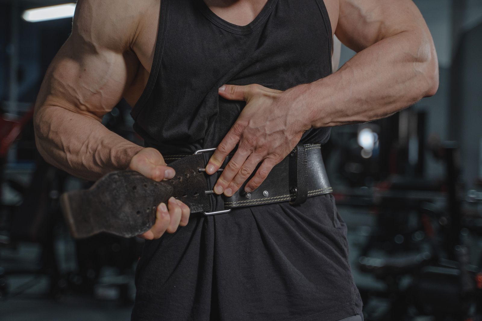 A lifter fastening a black leather weightlifting belt with a dual-prong buckle around the waist